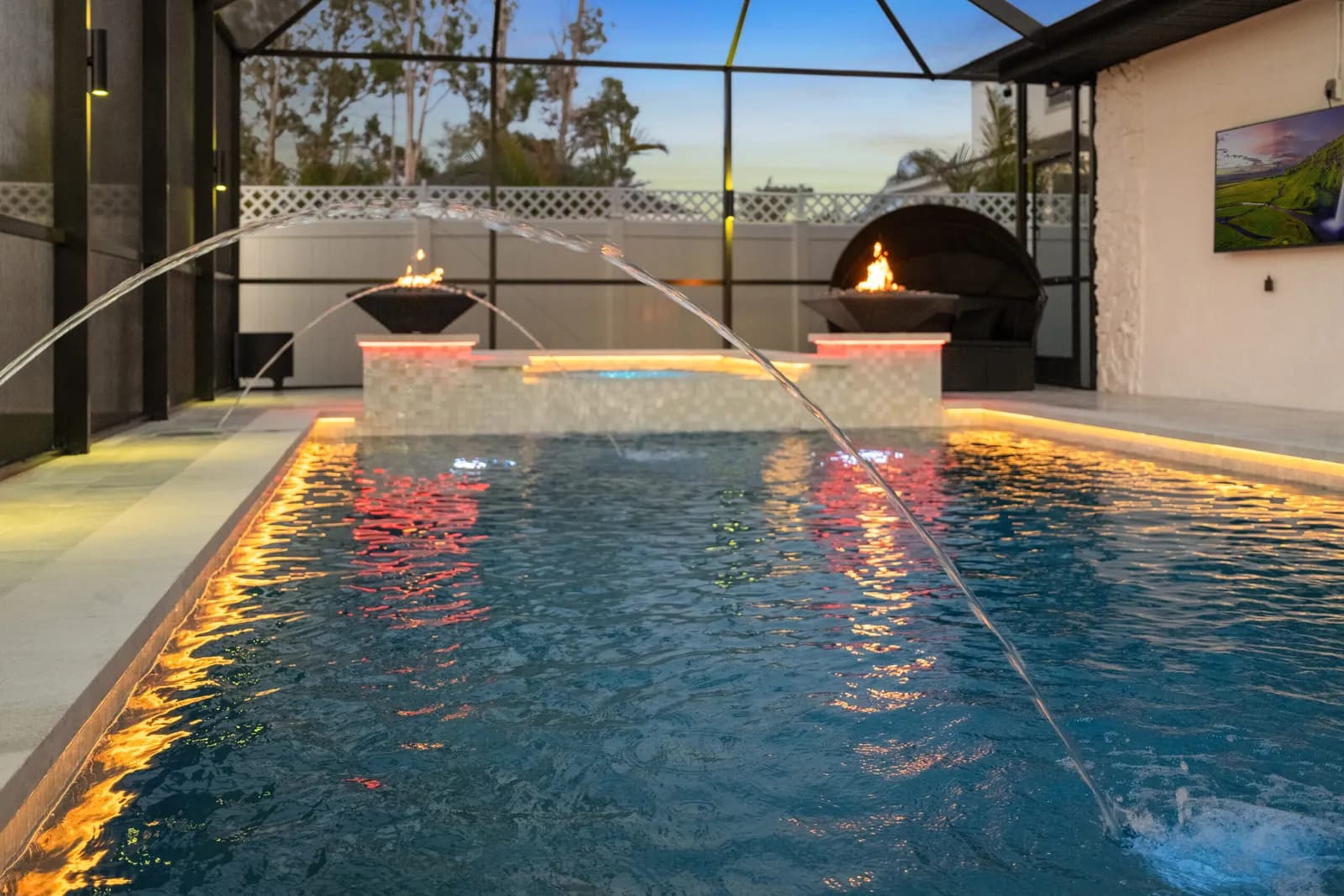 Tampa Bay pool at dusk with color-change LED edge lighting, lit deck jets, and fire bowls by LIV Pools